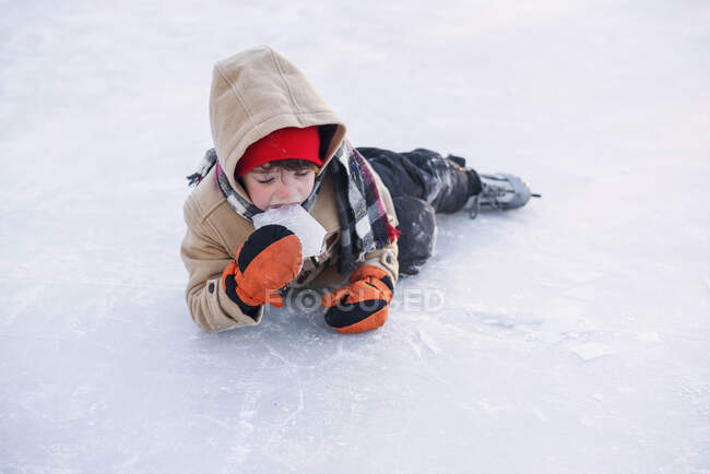 Menino deitado em um lago congelado usando patins de gelo comendo gelo — Fotografia de Stock