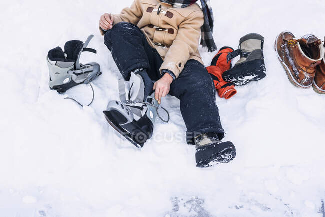 Мальчик, сидящий в снегу и надевающий коньки — стоковое фото