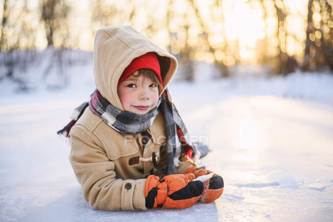 Porträt eines lächelnden Jungen, der auf einem zugefrorenen See liegt — Stockfoto