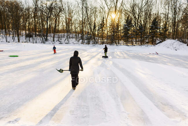 Mère et père déneigeant un lac gelé avec leur fils — Photo de stock