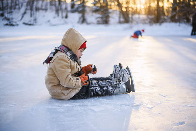 Menino sentado em um lago congelado usando patins no gelo — Fotografia de Stock