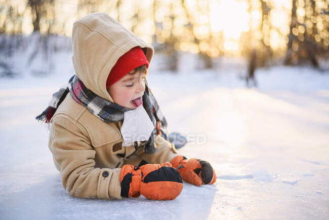 Ragazzo sdraiato su un lago ghiacciato leccare un pezzo di ghiaccio — Foto stock