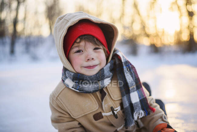 Retrato de um menino sorridente sentado em lago congelado — Fotografia de Stock