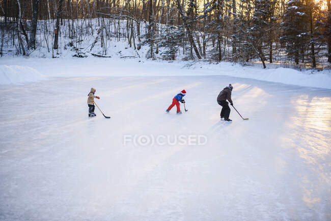Padre jugando hockey sobre hielo con sus dos hijos - foto de stock