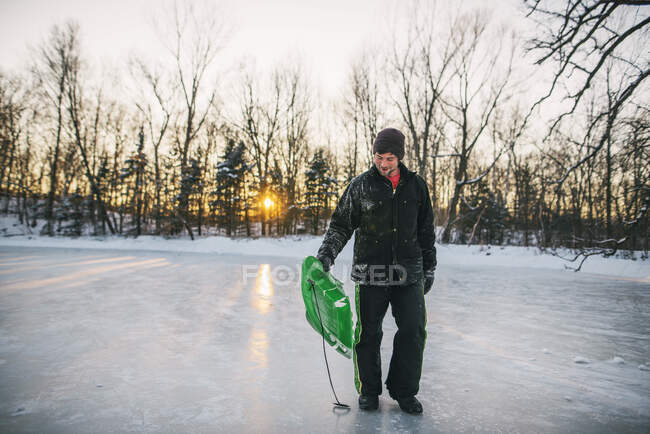 Hombre parado en un lago congelado sosteniendo un trineo - foto de stock