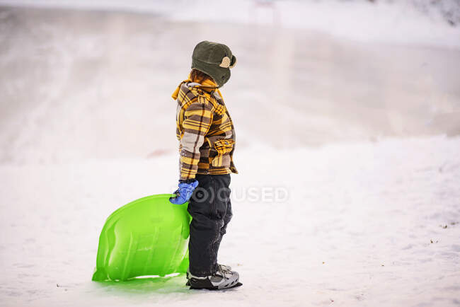 Boy standing on frozen lake holding a sledge — Stock Photo
