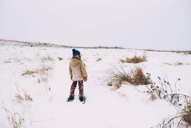 Boy walking in the snow wearing snowshoes — Stock Photo