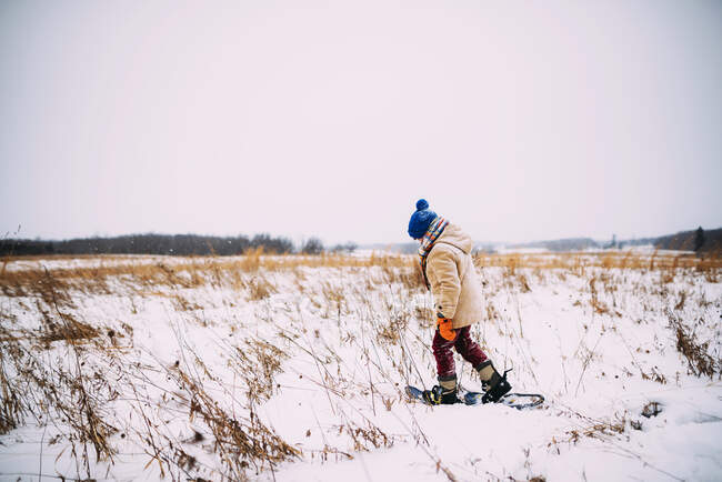 Мальчик ходит по снегу в снегоступах — стоковое фото
