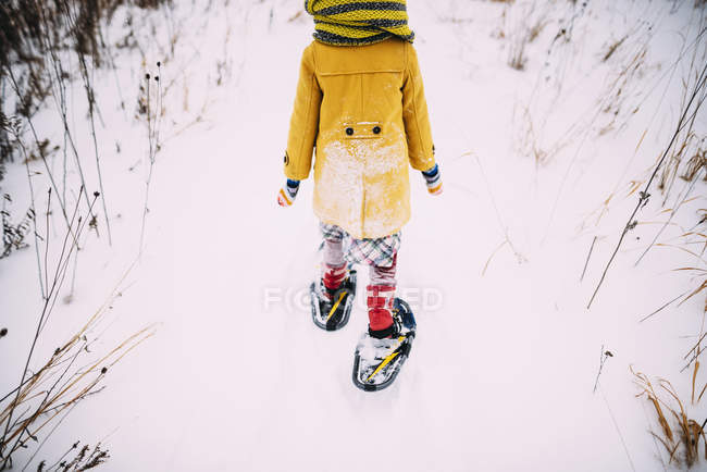Fille marchant dans la neige portant des raquettes — Photo de stock