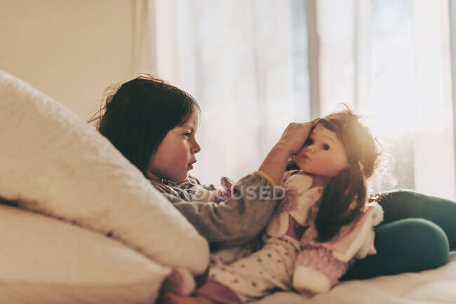Menina sentada em sua cama brincando com uma boneca — Fotografia de Stock