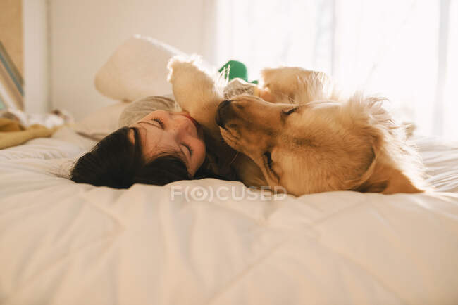 Дівчина лежить на ліжку зі своїм золотим собакою-ретривером — стокове фото
