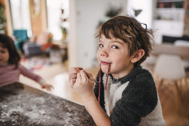 Retrato de un niño parado en la cocina comiendo pasta fresca - foto de stock