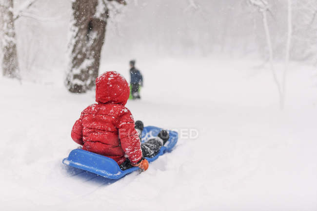 Vista trasera del niño trineo en la nieve pesada - foto de stock