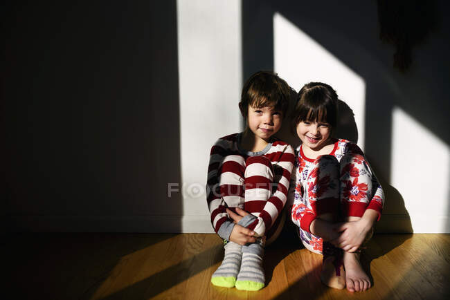 Мальчик и девочка в пижаме, сидящие на полу, купающиеся в солнечном свете — стоковое фото