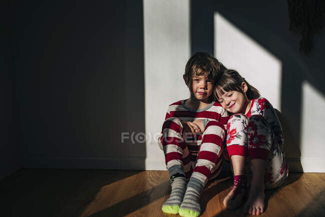 Garçon et fille en pyjama assis sur le sol baigné de lumière du soleil — Photo de stock