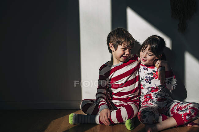 Niño y niña sentados en el suelo abrazándose - foto de stock
