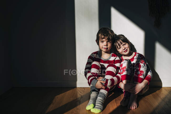 Garçon et fille en pyjama assis sur le sol baigné de lumière du soleil — Photo de stock