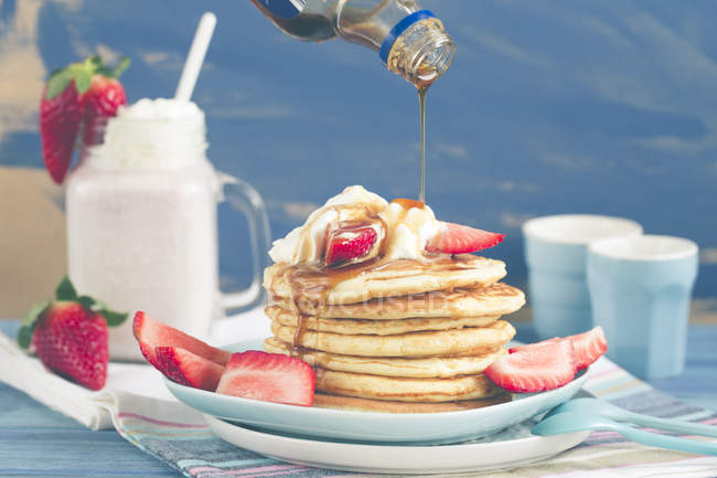 Pouring syrup onto a Stack of pancakes with fresh strawberries — Stock Photo