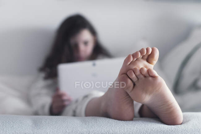 Chica sentada en la cama usando una tableta digital - foto de stock