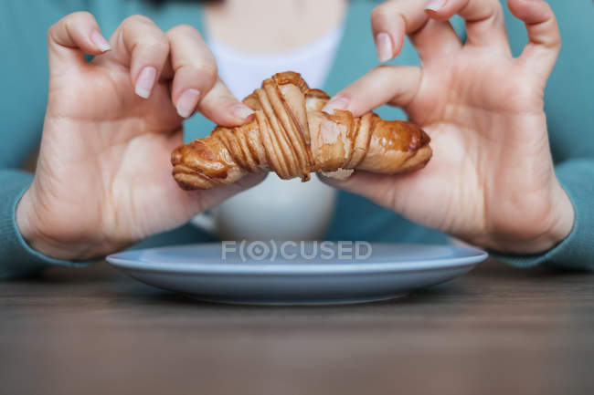 Imagen recortada de las manos de mujer sosteniendo un croissant - foto de stock