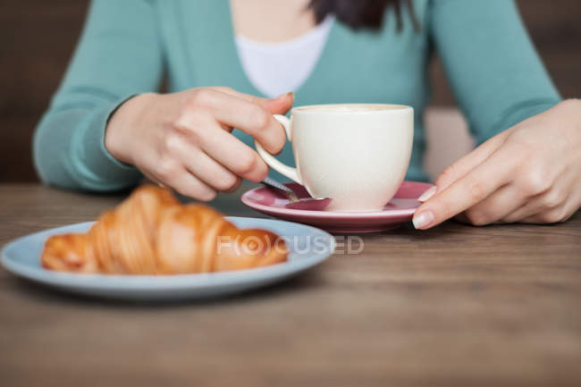 Frau hält Tasse Kaffee, frisches Croissant auf einem Teller — Stockfoto