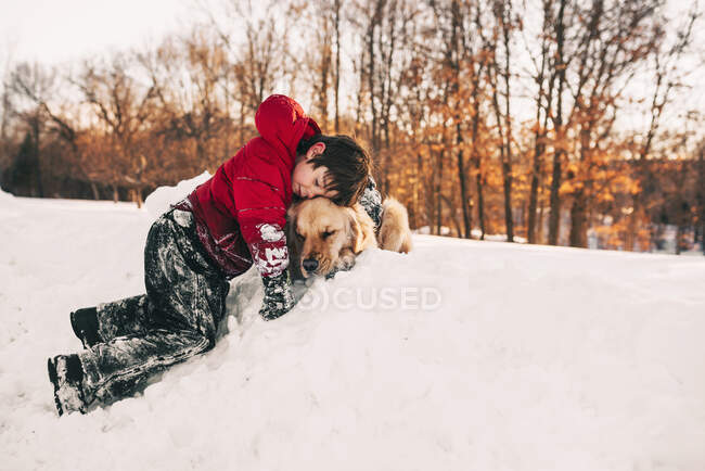Мальчик обнимает свою золотую собаку-ретривер в снегу — стоковое фото