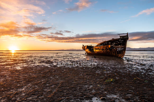 Разрушенная лодка на закате над морем — стоковое фото