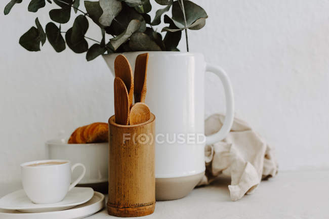Tasse à café, croissant, ustensiles de cuisine et eucalyptus dans une cruche — Photo de stock