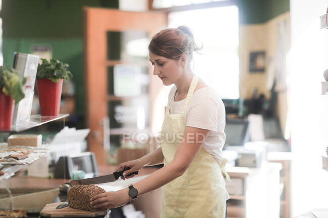 Sales assistant cutting a loaf of bread in half — Stock Photo