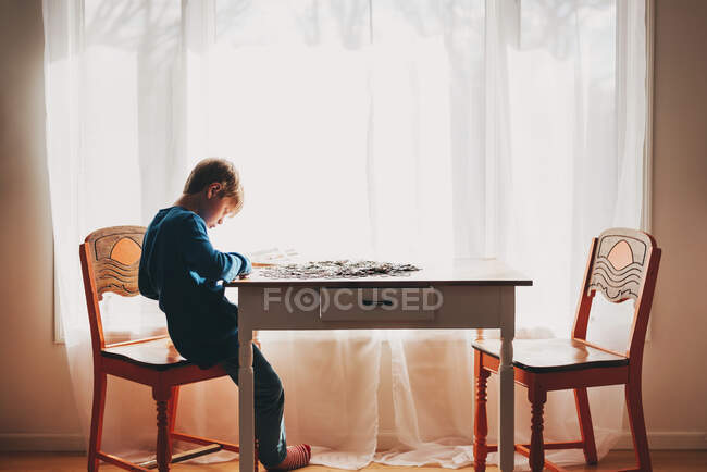 Menino sentado em uma mesa fazendo um quebra-cabeça — Fotografia de Stock