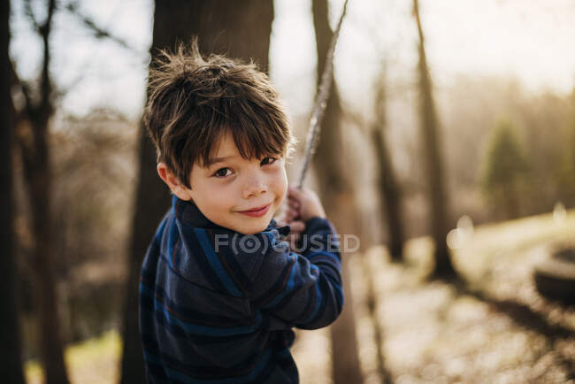 Мальчик играет на веревке качели в лесу — стоковое фото