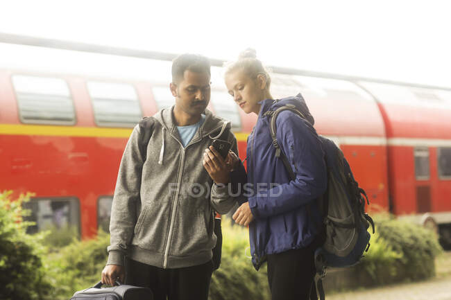 Couple standing on a train platform looking at a mobile phone — Stock Photo