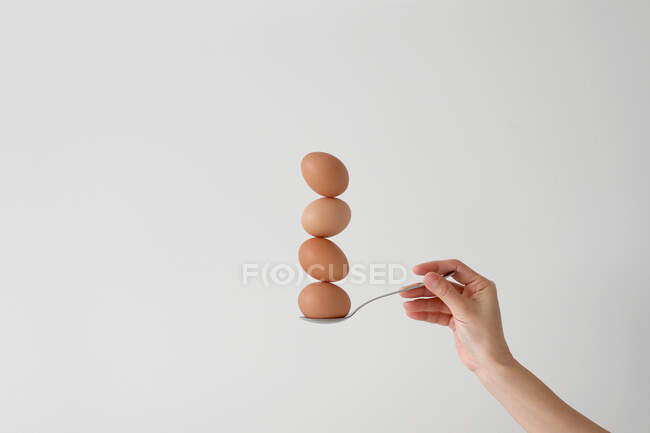 Mano de mujer sosteniendo una cuchara con cuatro huevos balanceándose uno encima del otro - foto de stock