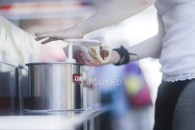 Женщина добавляет соус карри в хот-дог — стоковое фото