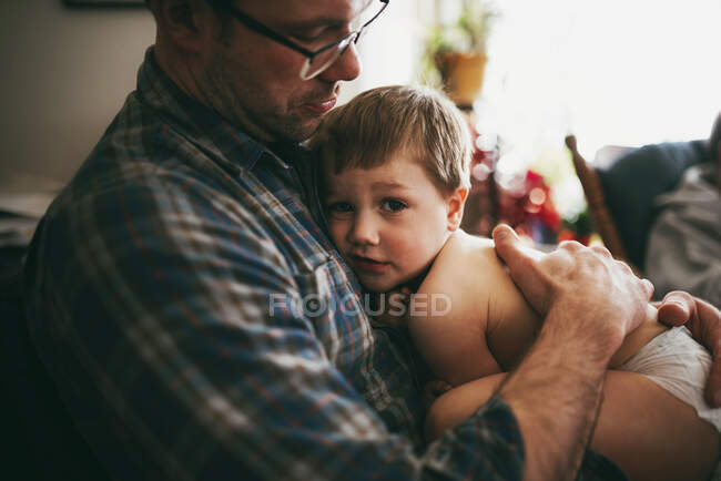 Батько сидить на дивані, пригорнувши сина і цілуючи його на голові — стокове фото