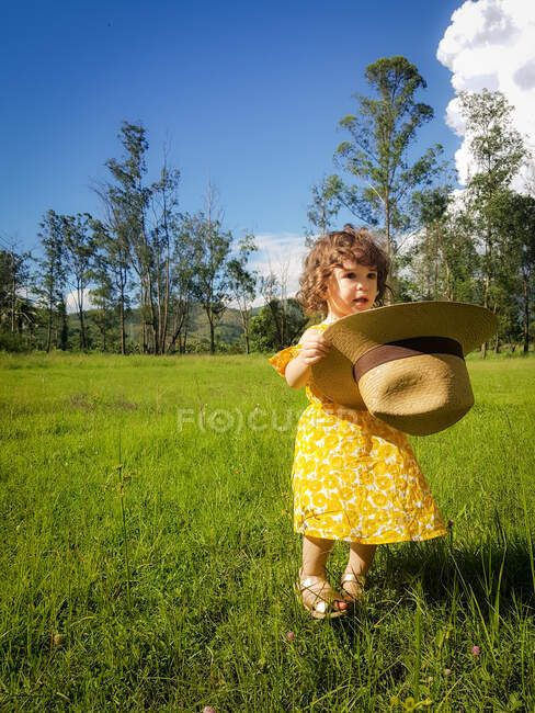 Girl standing in a field holding a summer hat, Brazil — Stock Photo