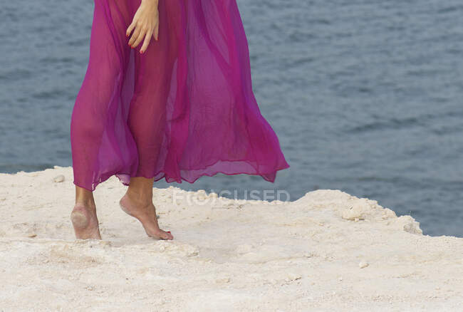 Обрезанный снимок женщины в розовом платье, гуляющей по пляжу — стоковое фото