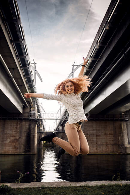 Mujer saltando en el aire por un río, Bélgica - foto de stock