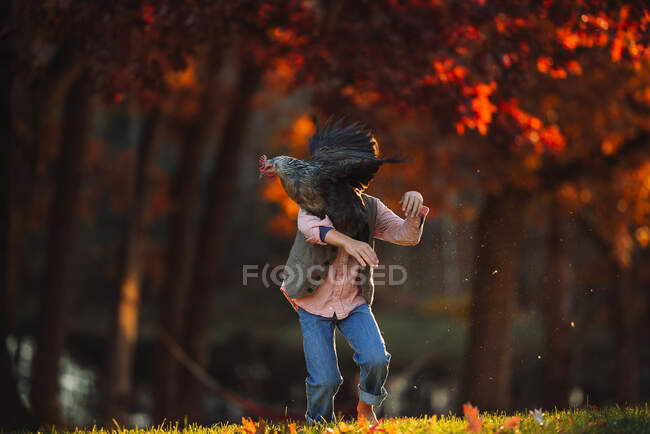 Chico parado al aire libre jugando con un pollo, Estados Unidos - foto de stock