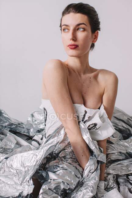Жінка в паперовій сукні сидить на срібній фользі — стокове фото
