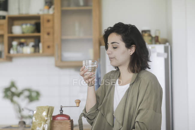 Woman standing in the kitchen drinking a glass of water — Stock Photo