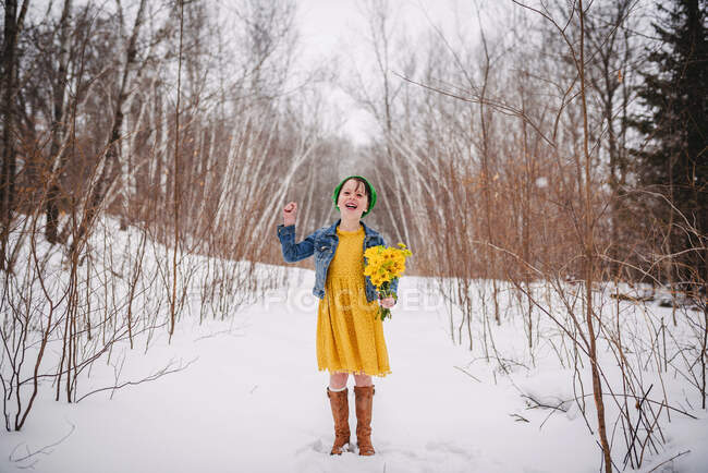 Sonriente chica de pie en la nieve sosteniendo un ramo de flores - foto de stock