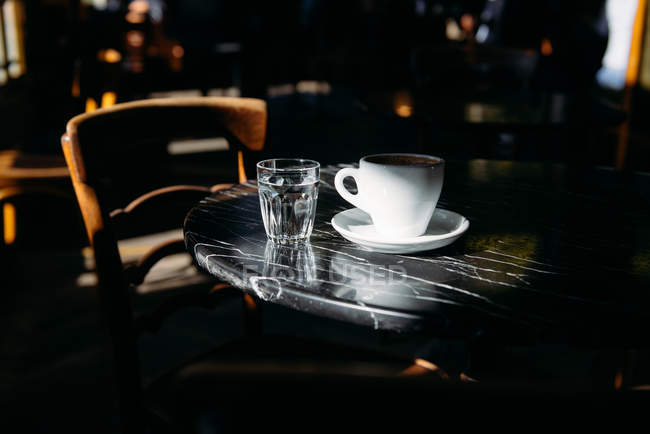 Close-up of a cup of coffee and glass of water on a table — Stock Photo