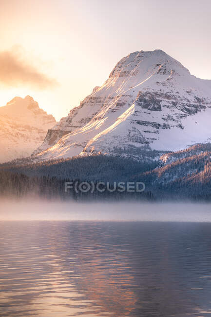 Hermosa vista del lago y las rocas nevadas al atardecer - foto de stock
