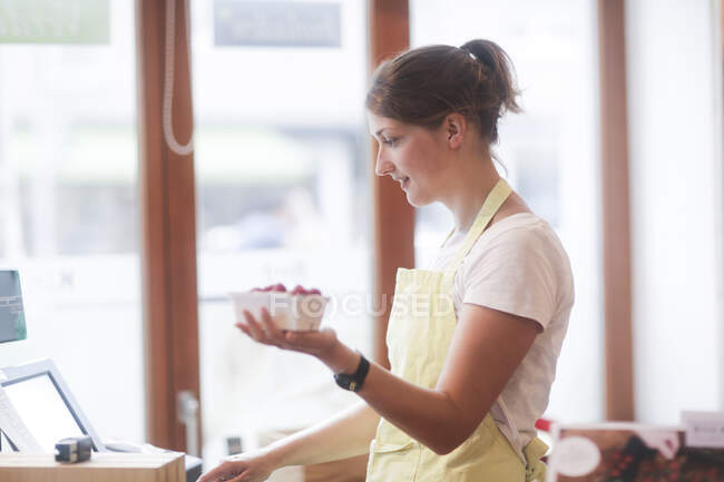 Assistente de vendas numa caixa registadora com um punnet de morangos — Fotografia de Stock