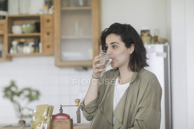 Woman standing in the kitchen drinking a glass of water — Stock Photo