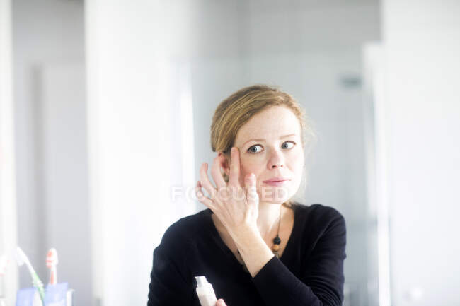Femme debout dans la salle de bain appliquant maquillage — Photo de stock