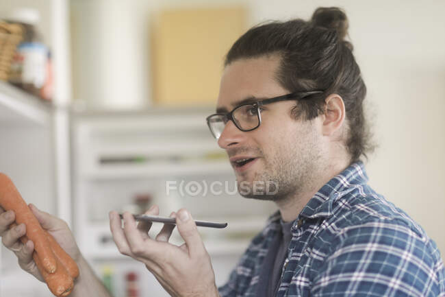 Portrait of a man holding carrots talking into a mobile phone — Stock Photo