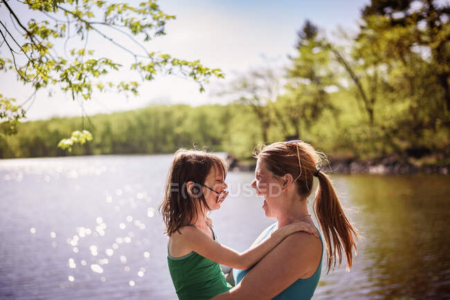Mother standing by a lake carrying her daughter — Stock Photo