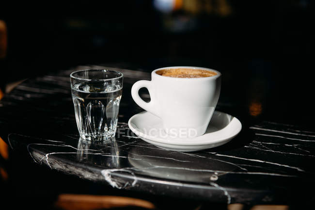 Gros plan d'une tasse de café et d'un verre d'eau sur une table — Photo de stock